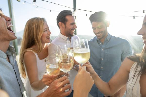A group of friends cheers their white wine while laughing