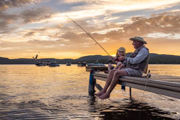 A grandpa and grandchild fish from a dock