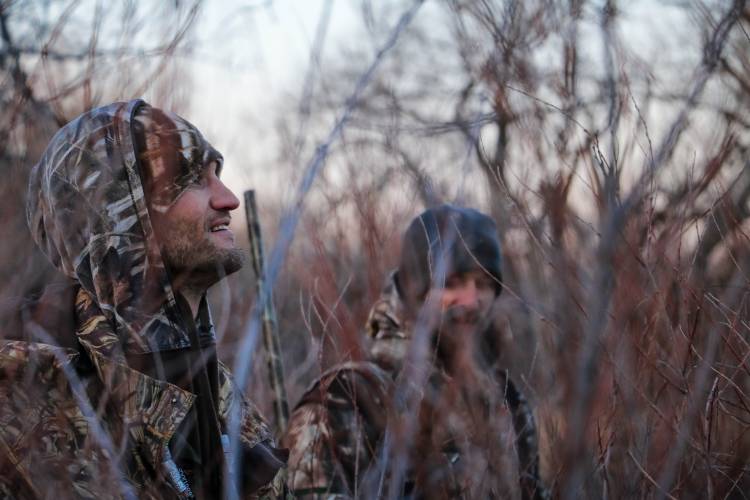 Two duck hunters talk in the reeds by water