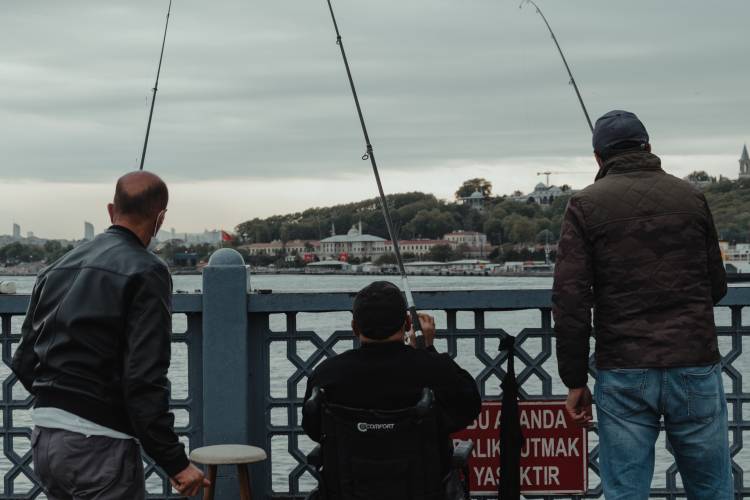 Three people reel in a fish on a pier